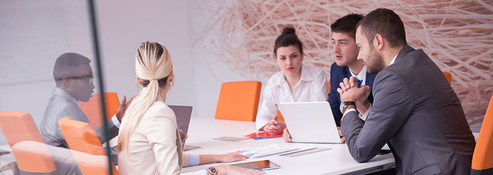 A group of people discussing something, seated, in a conference room. 