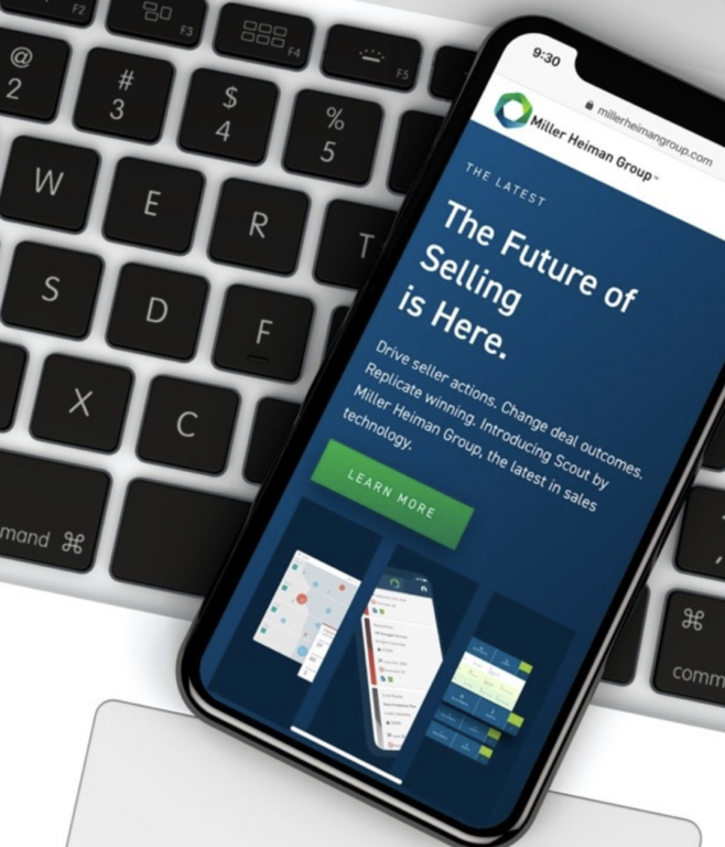 a smartphone displaying the new Miller Heiman Group website with the tagline "the future of selling is here," resting on a laptop keyboard