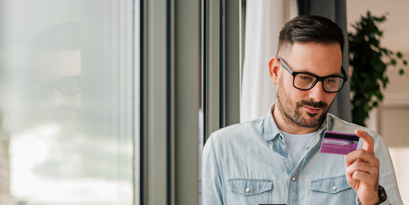 Man in glasses sitting by window looking at credit card