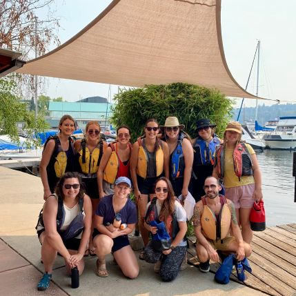 A group of people smiling for a photo while wearing life jackets before they go kayaking