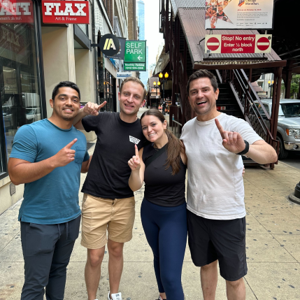Four people hold up one finger to showcase first place after winning a scavenger hunt