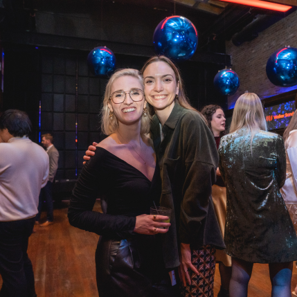 Two women smile at the camera at a company holiday party