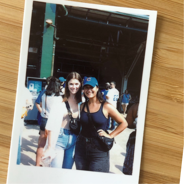 A picture of a polaroid on a desk, showing two women smiling at a cubs game outside the stadium