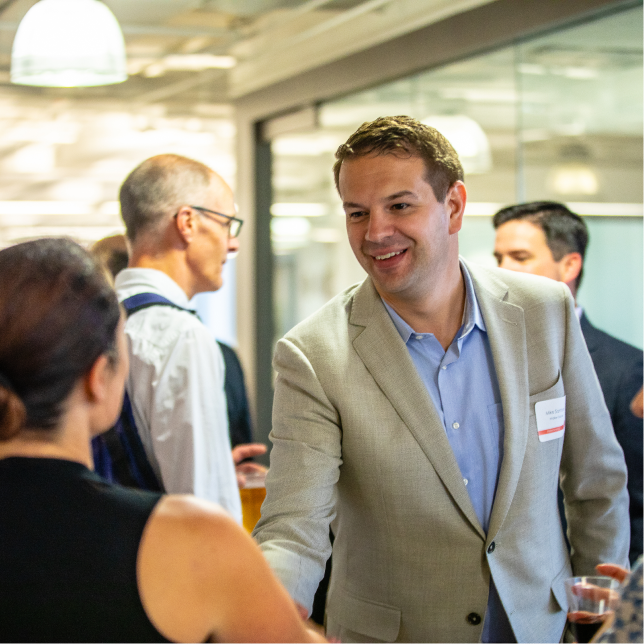 A man smiling while shaking a woman's hand and introducing himself