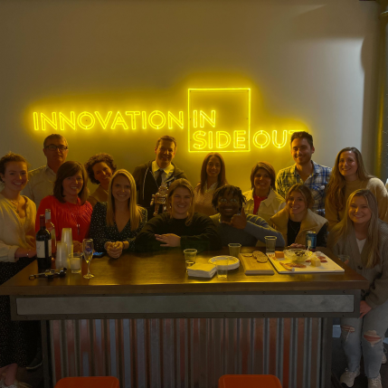 Group of people posing behind a bar in front of an LED sign that says "Innovation Inside Out"