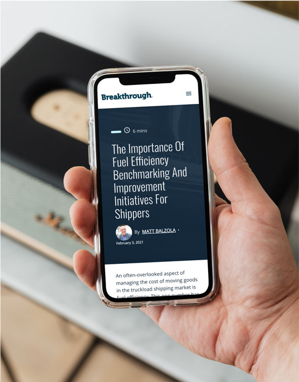 a hand holding a smartphone showing a breakthrough blog post titled "the importance of fuel efficiency benchmarking and improvement initiatives for shippers"