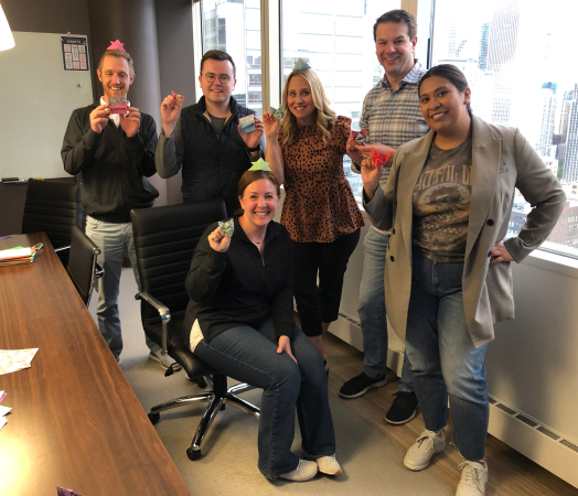 six people in a conference room smiling and holding origami