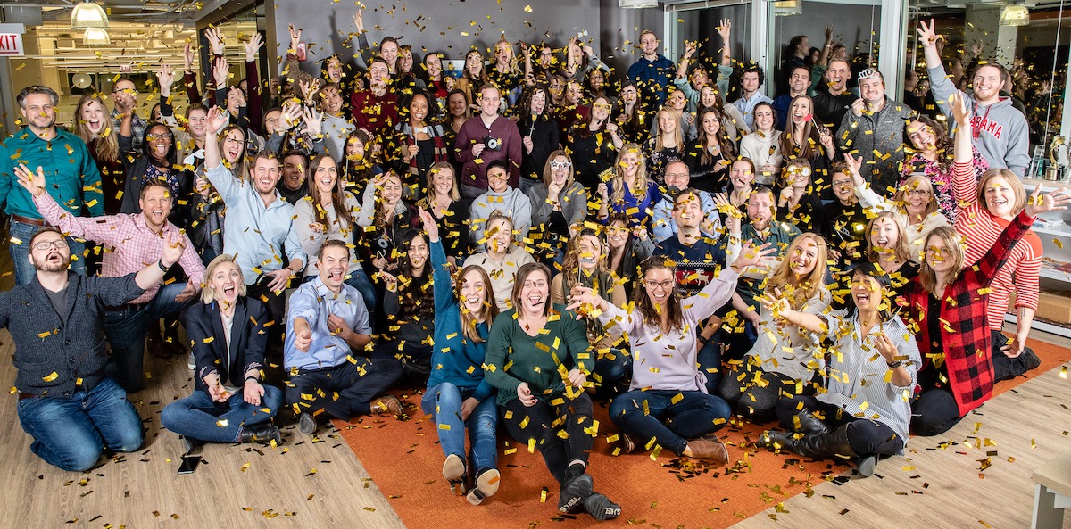 Portrait of Walker Sands employees throwing gold confetti in the air in the office
