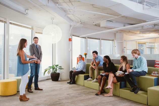 Two employees standing in front of five employees who are seated on bleachers in front of them in an office