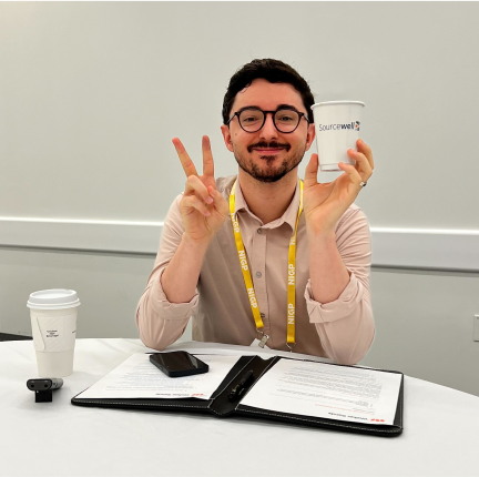 Man with pink shirt making a peace sign with his fingers and holding up a Sourcewell branded cup