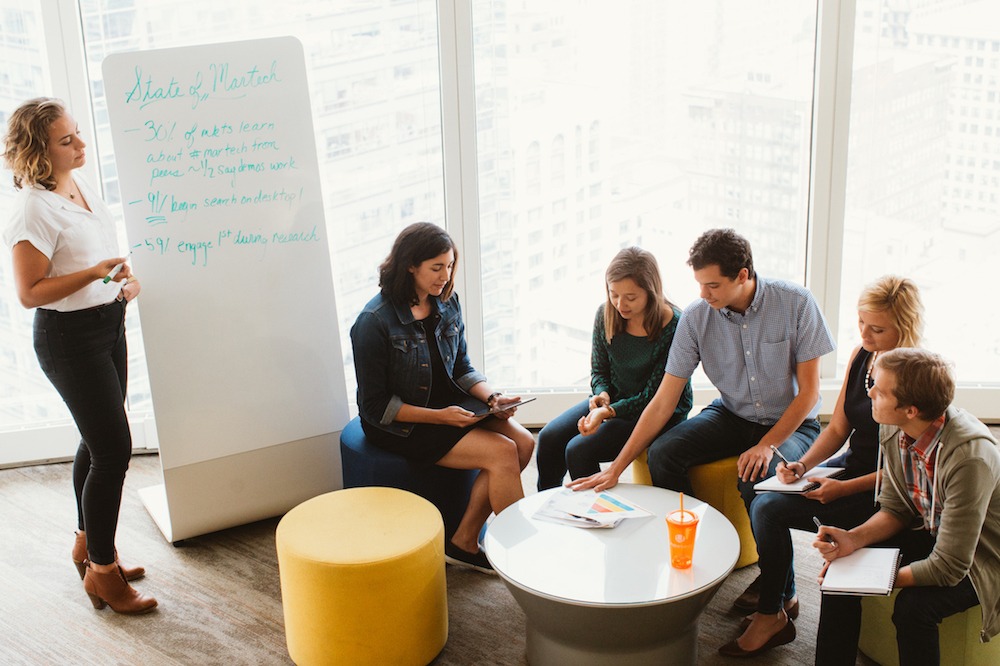 Group of coworkers gathered around a table and whiteboard at a brainstorm meeting