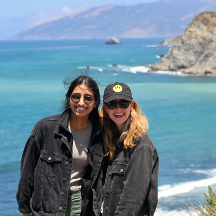 Two women in sunglasses smiling in front of an ocean. 