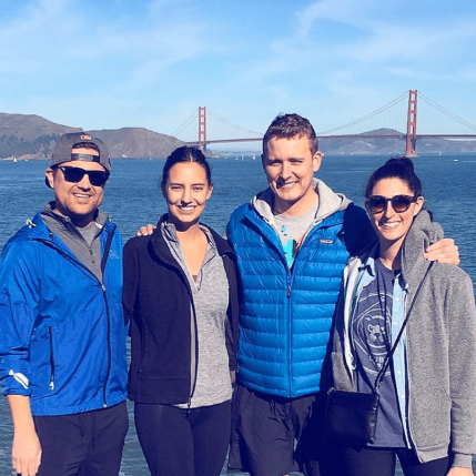 Four people smiling in front of the Golden Gate bridge. 