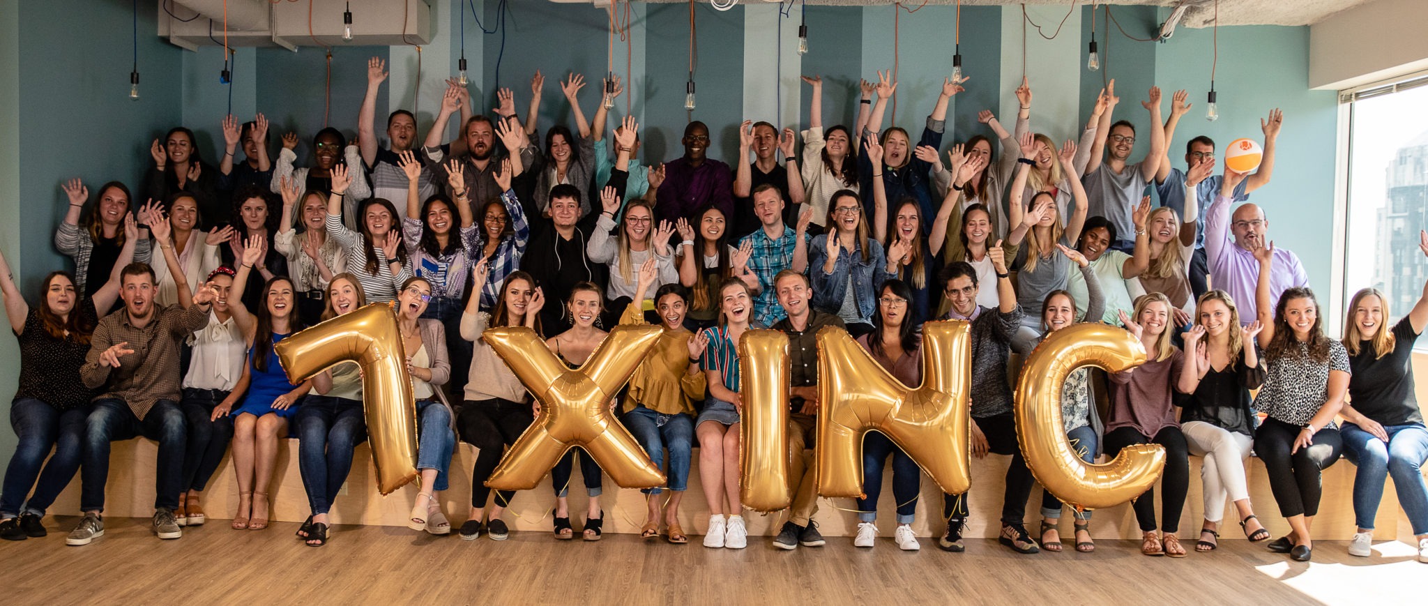 Portrait of Walker Sands employees sitting on bleachers behind balloons that say "7 X INC" 