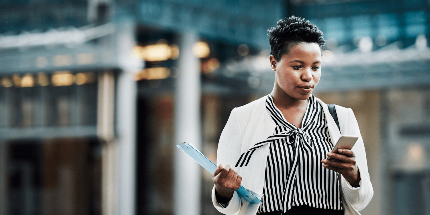 Woman wearing white blazer standing outside holding phone 