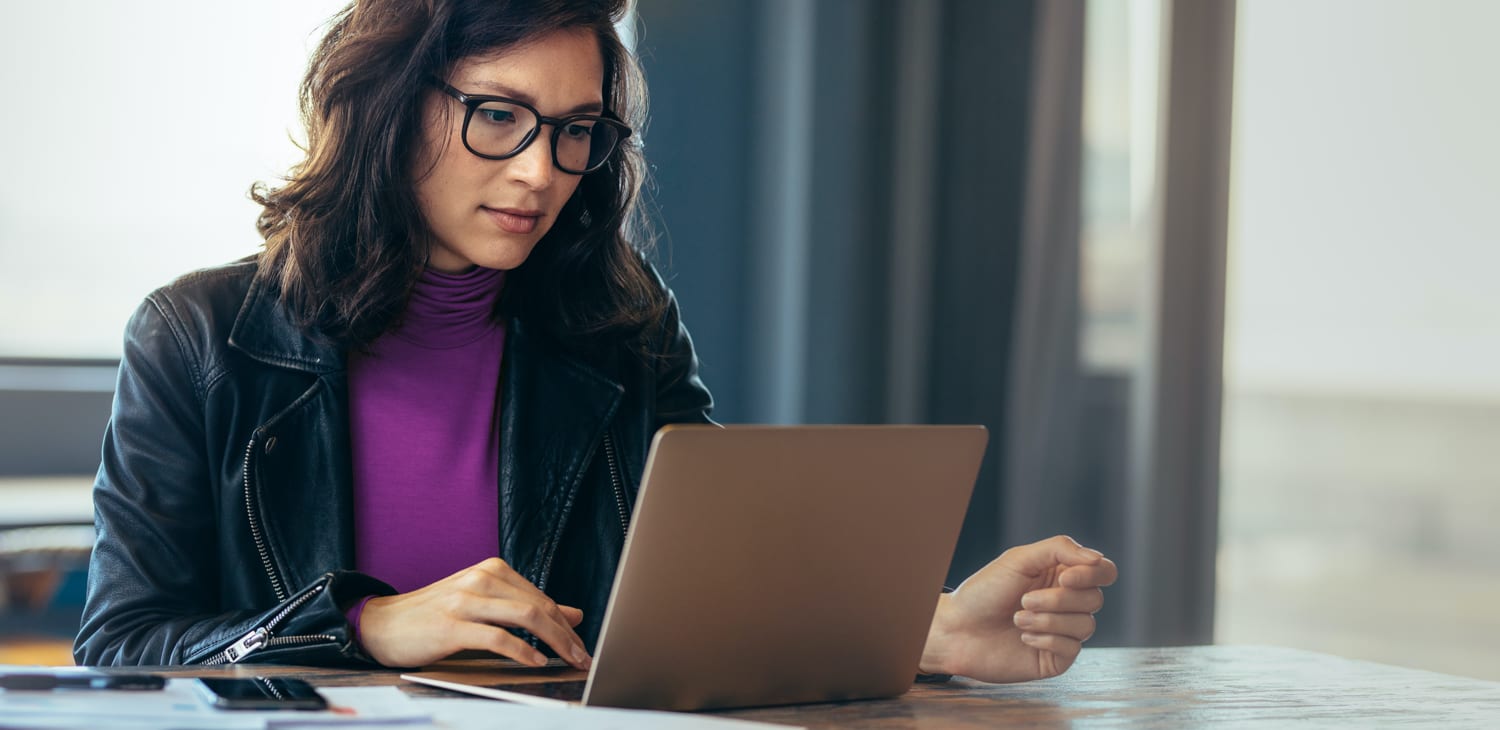 a woman with glasses and a purple shirt looking at a laptop