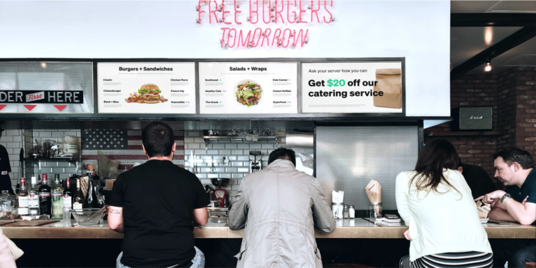 Four people sitting at a casual restaurant counter with an UPshow ad displayed on the menu