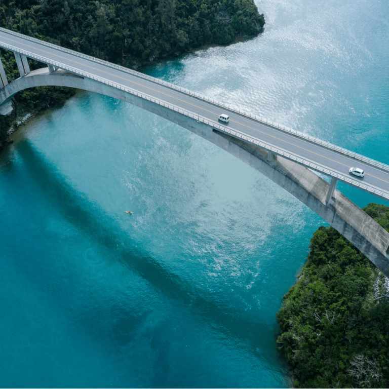 aerial view of two cars driving on a bridge above bright blue water