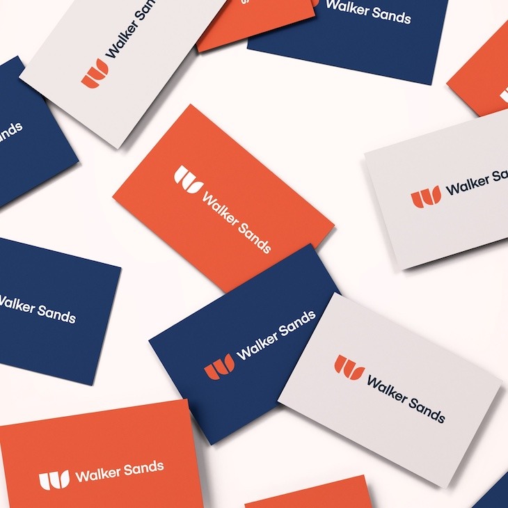 Orange, dark blue and white Walker Sands business cards scattered on a white tabletop