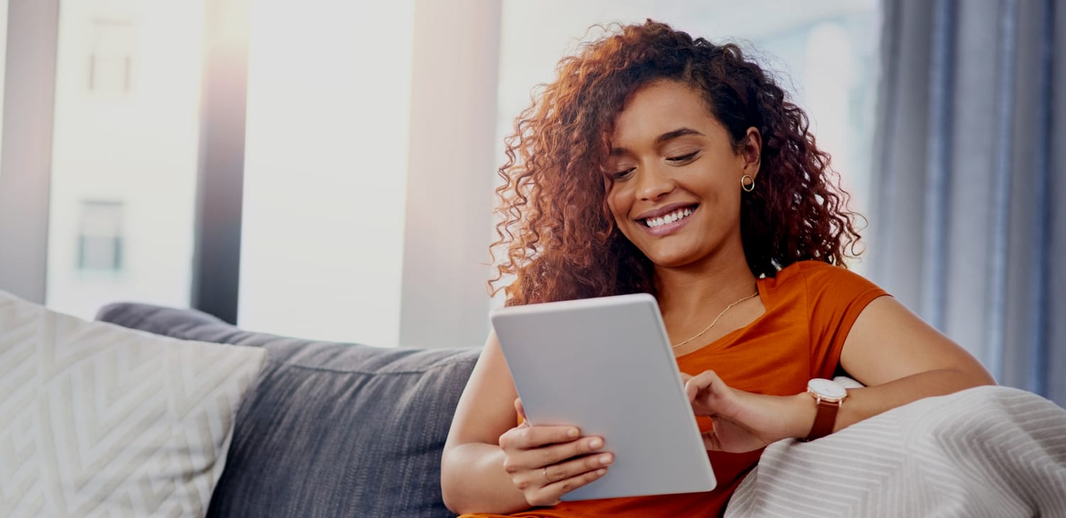 a smiling woman sits on a couch holding an ipad