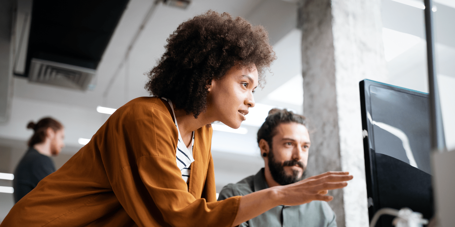 a man and a woman looking at a computer monitor together while the woman gestures